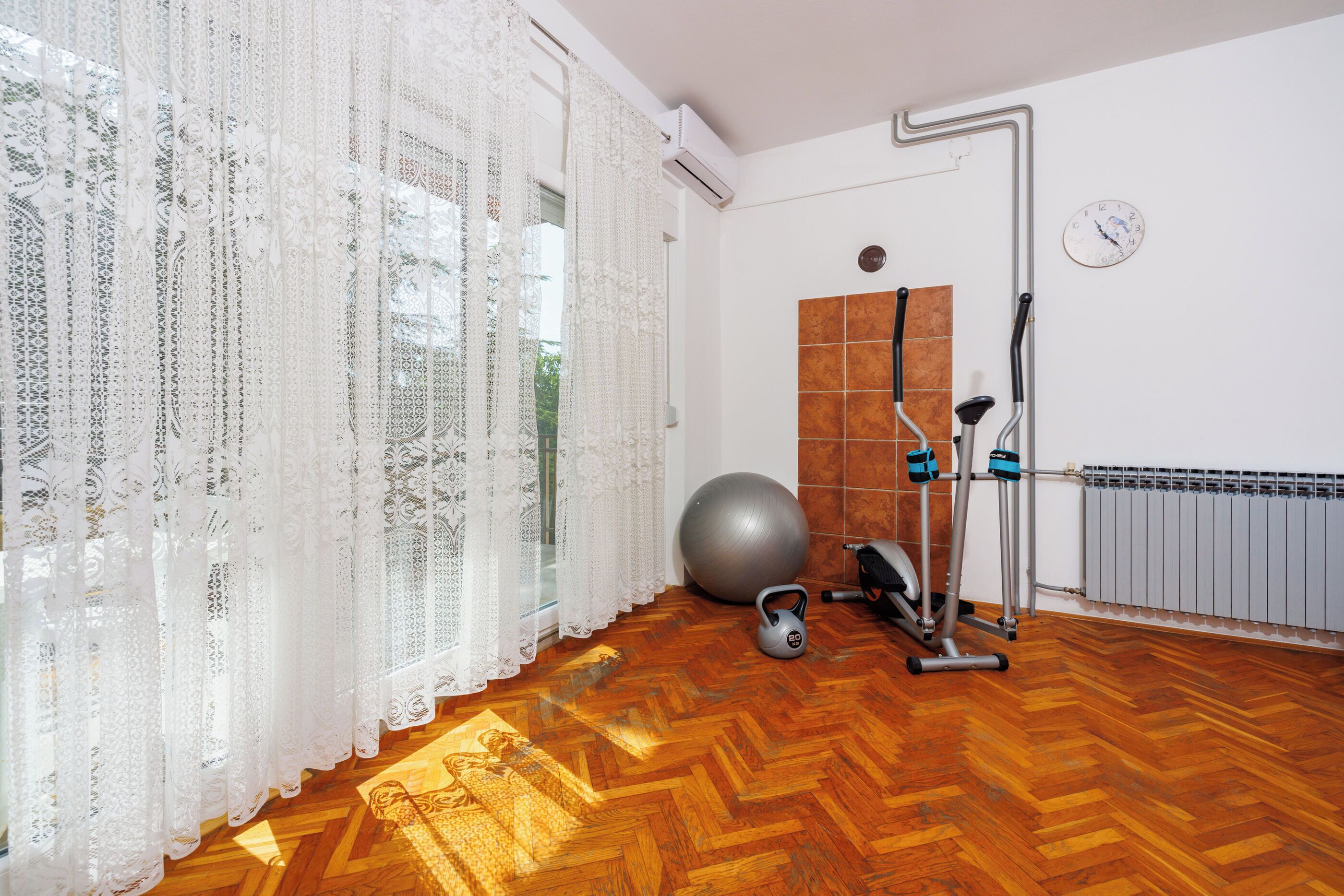 A room with a wooden herringbone floor, a large exercise ball, a kettlebell, and a stationary bike.