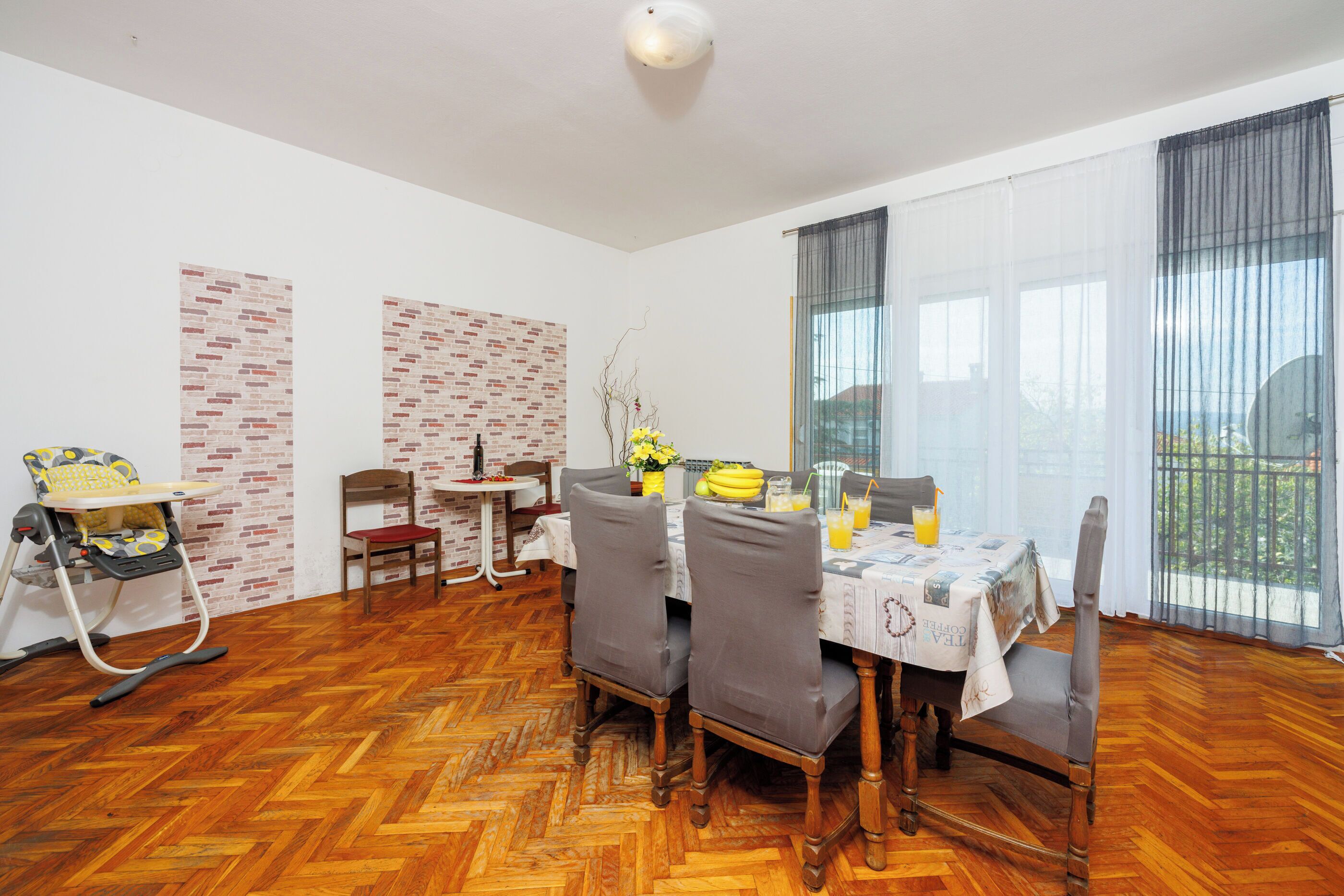Un espace repas doté d’un parquet en bois disposé en point de Hongrie, d’une table entourée de chaises et offrant une vue sur l’extérieur grâce à de grandes fenêtres.