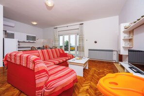 A modern living room with a red sofa, a white coffee table, and a view of the outdoors through large windows. - Apartments Davorka (Crikvenica)