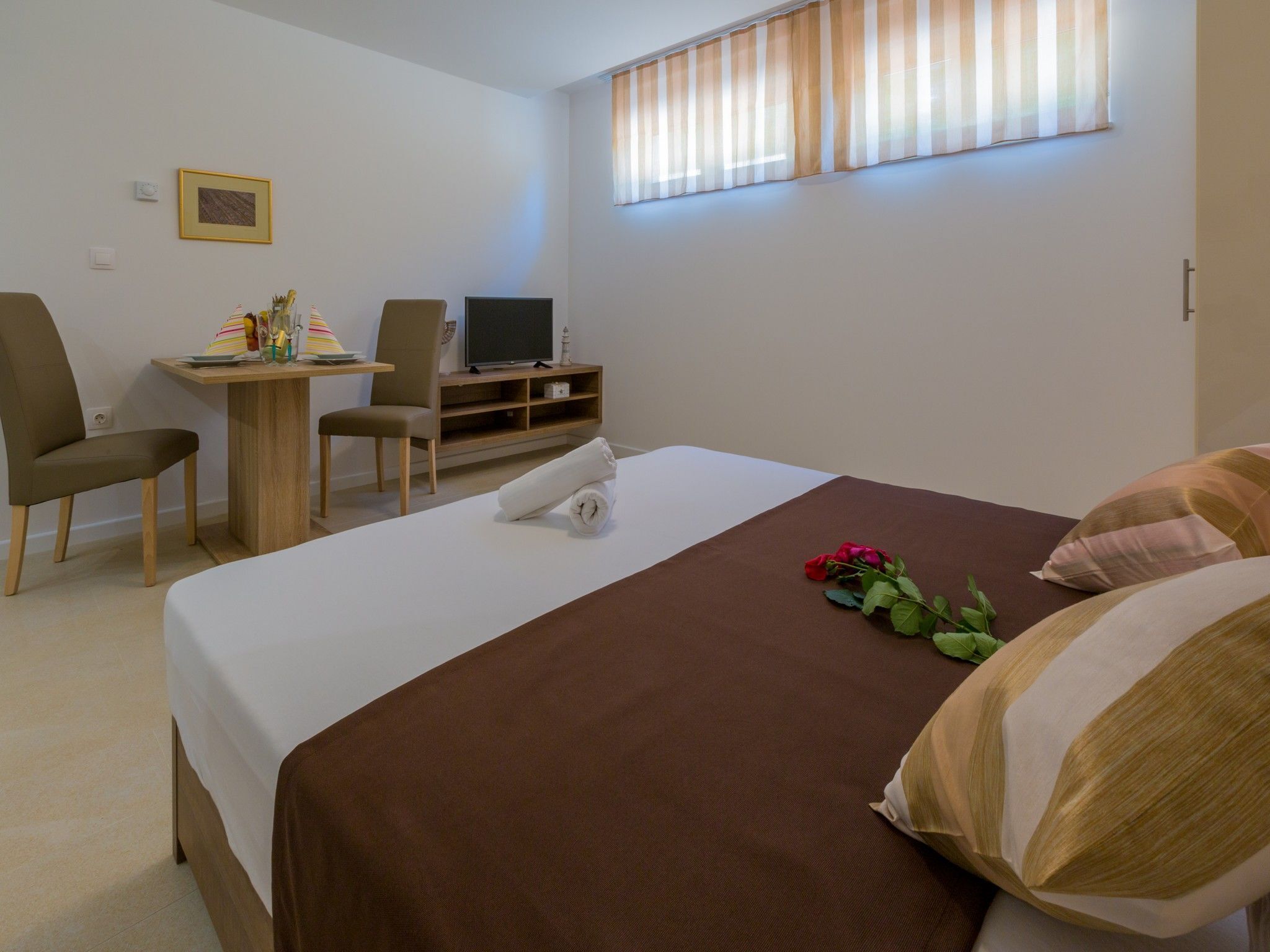 A hotel room with a bed, a desk with a computer, a chair, and a window with curtains.