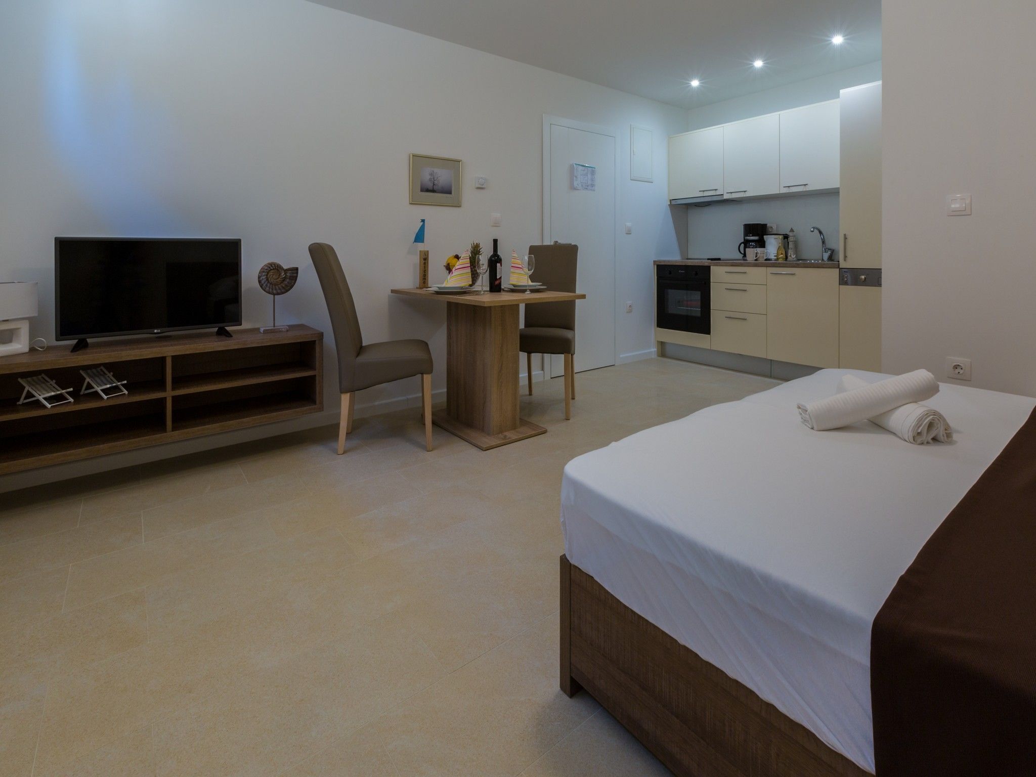 A hotel room with a bed, a TV, a desk, and a kitchenette.