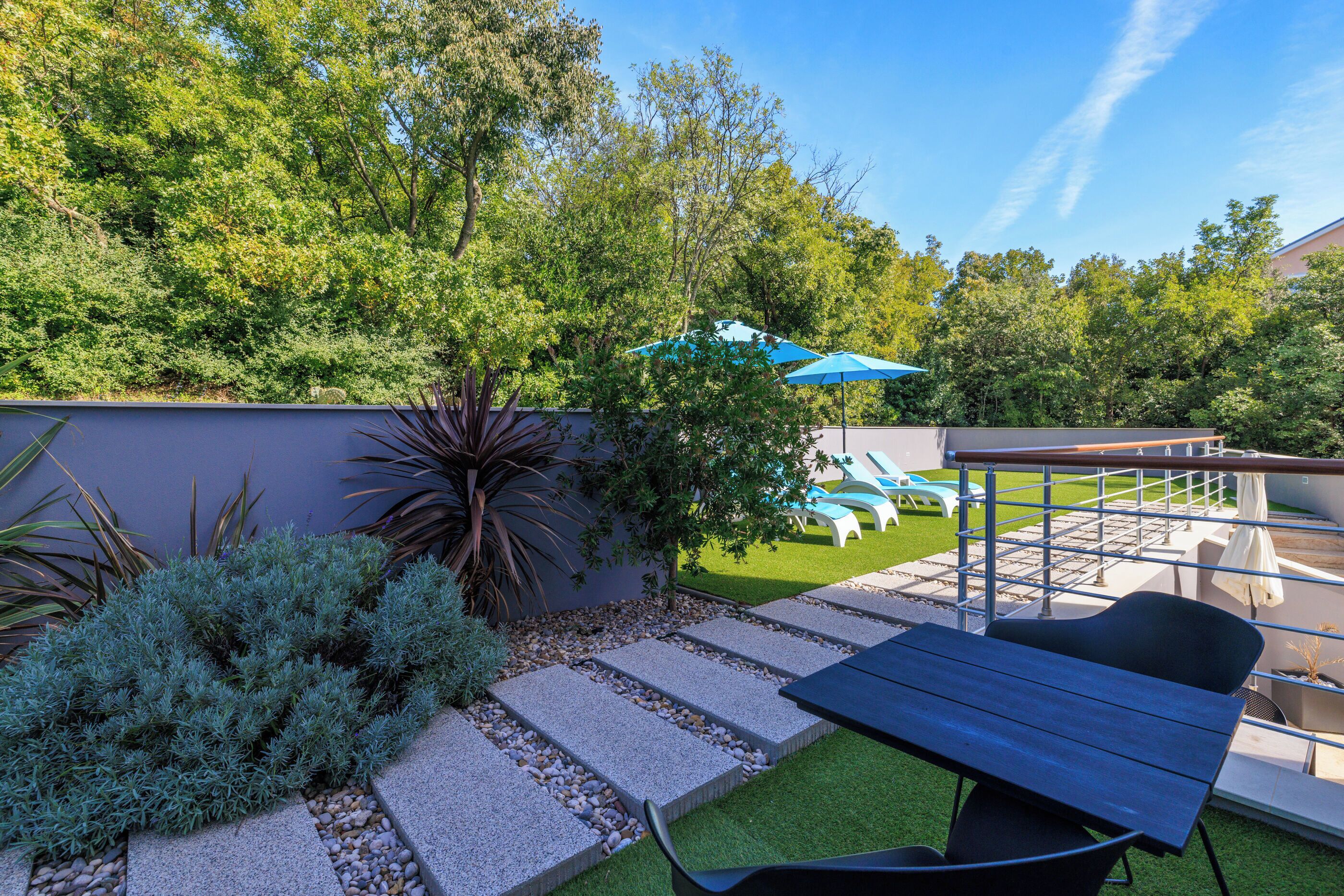 A patio with a table and chairs, surrounded by a garden with a stone pathway and various plants.