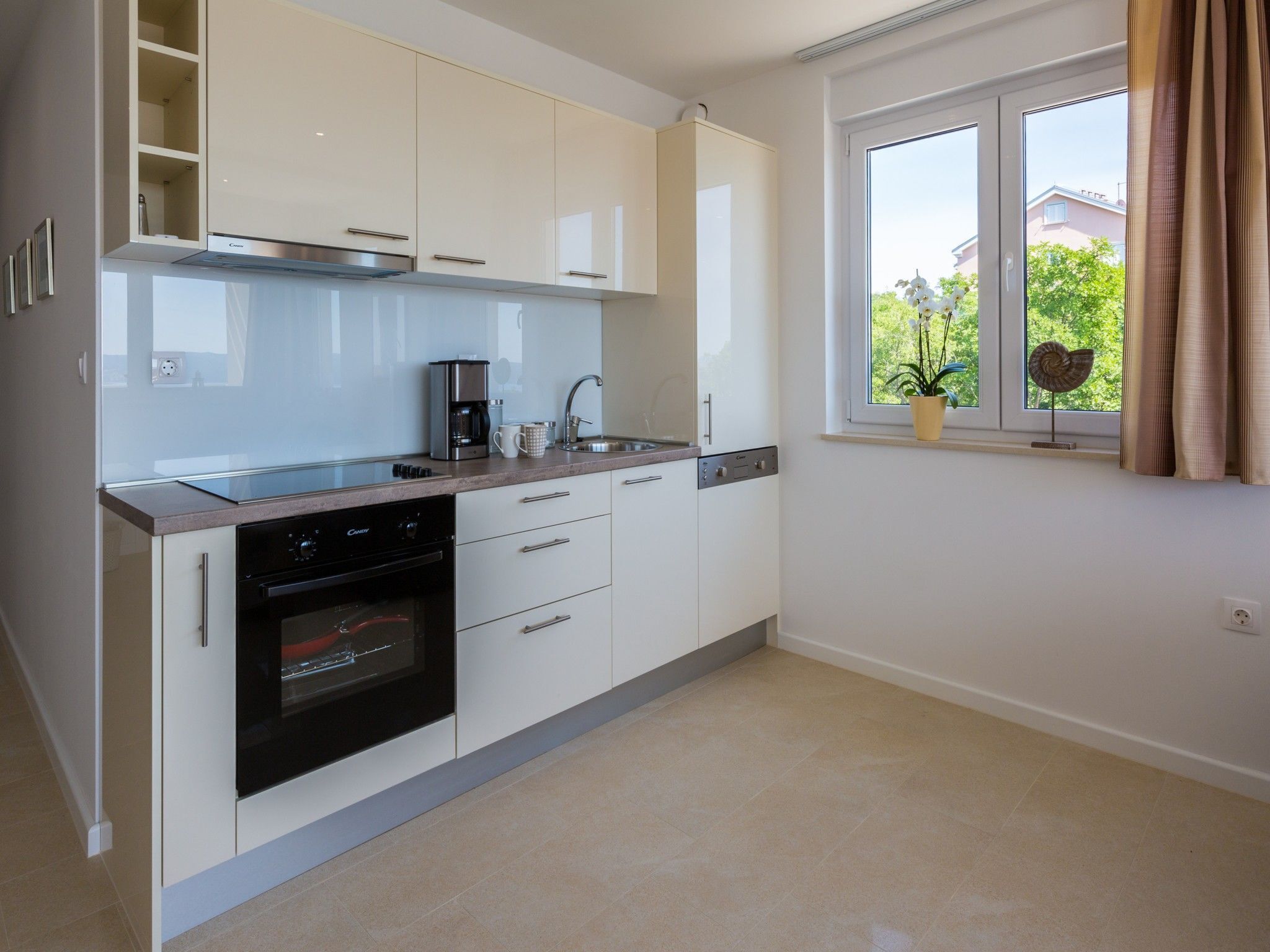 A modern kitchen with white cabinets, a built-in oven, a coffee maker, and a window with a view of greenery.