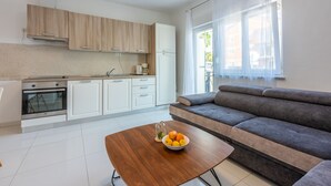 Una cocina moderna con armarios blancos, un horno empotrado y una zona de comedor con mesa de madera y un tazón de fruta.