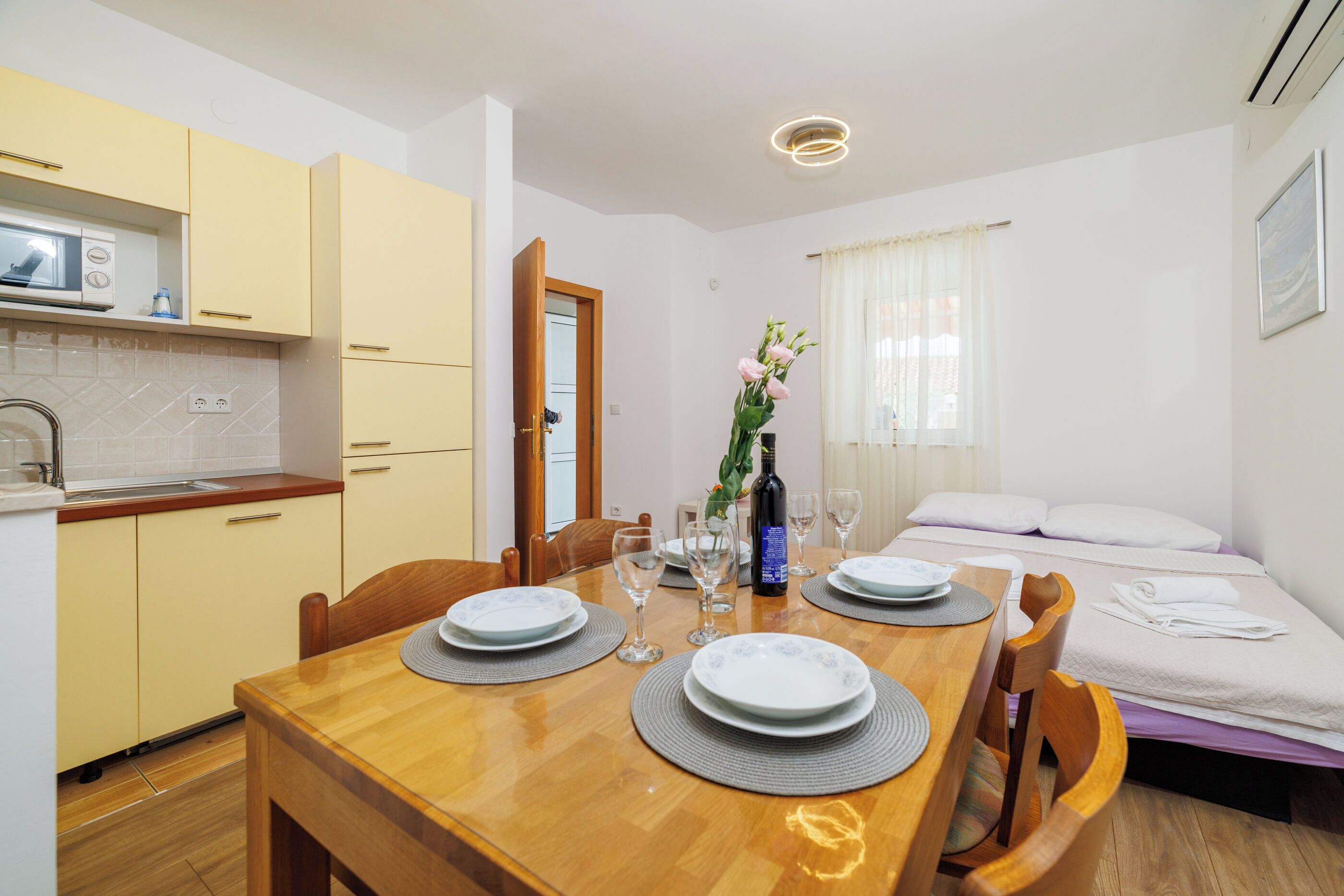 A compact hotel room with a dining area, kitchenette, and a bed with a white comforter.
