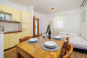 A compact hotel room with a dining area, kitchenette, and a bed with a white comforter. - Apartments Carmen (Crikvenica)