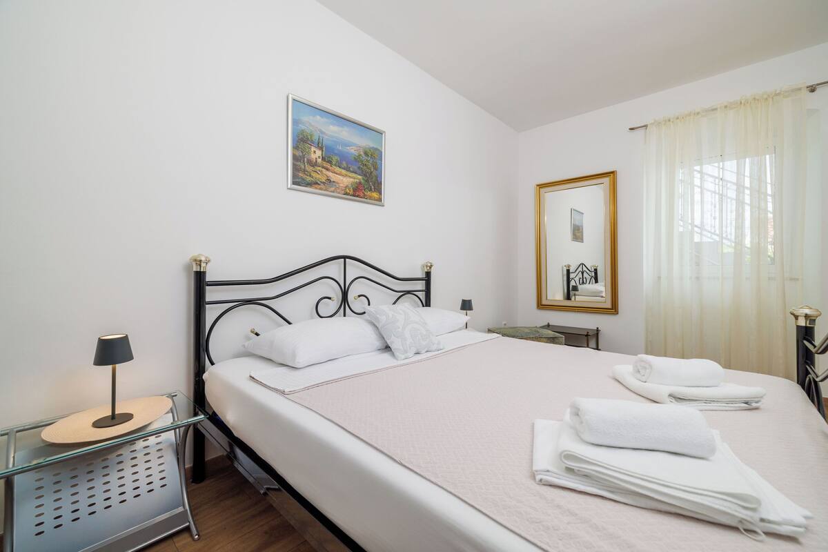 Un lit bien fait, avec du linge de lit blanc, une table de chevet avec une lampe, un tableau au mur et un miroir.