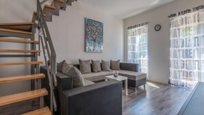 A modern living room with a staircase, a sofa set, a coffee table, and a large window with curtains. - Apartment IVA MAN (Crikvenica)
