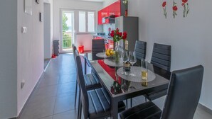 A modern kitchen with red cabinets, a dining area with a glass table, and a balcony with a red chair. - Apartment IVA MAN (Crikvenica)
