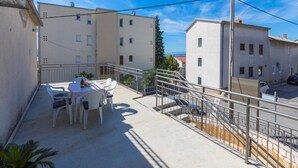A balcony with a table and chairs, a metal railing, and buildings in the background. - Apartment IVA MAN (Crikvenica)