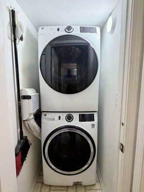 Un lavadero pequeño con lavadora y secadora apiladas, un aspirador y un calentador.