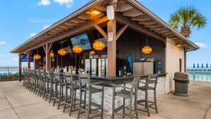 An outdoor bar area with a pool view, featuring wooden beams, bar stools, and hanging pendant lights. - 11th floor paradise! (Panama City Beach)