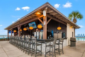 An outdoor bar area with a pool view, featuring wooden beams, bar stools, and hanging pendant lights. - 11th floor paradise! (Panama City Beach)