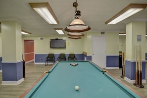 Une table de billard avec des billes, un téléviseur fixé au mur et plusieurs chaises.