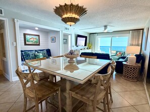 A dining area with a glass-top table, wooden chairs, and a decorative bowl centerpiece. - 11th floor paradise! (Panama City Beach)