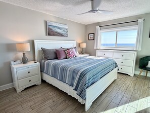 A bedroom with a bed, nightstands, a dresser, a ceiling fan, a window with curtains, and a painting on the wall.