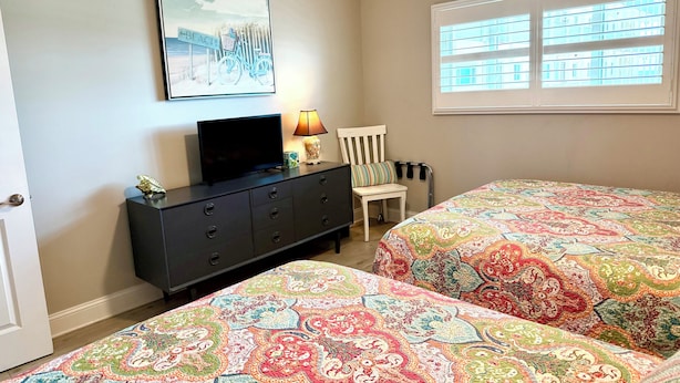 A bedroom with two beds, a dresser, a television, a lamp, a chair, and a window with blinds. - 11th floor paradise! (Panama City Beach)