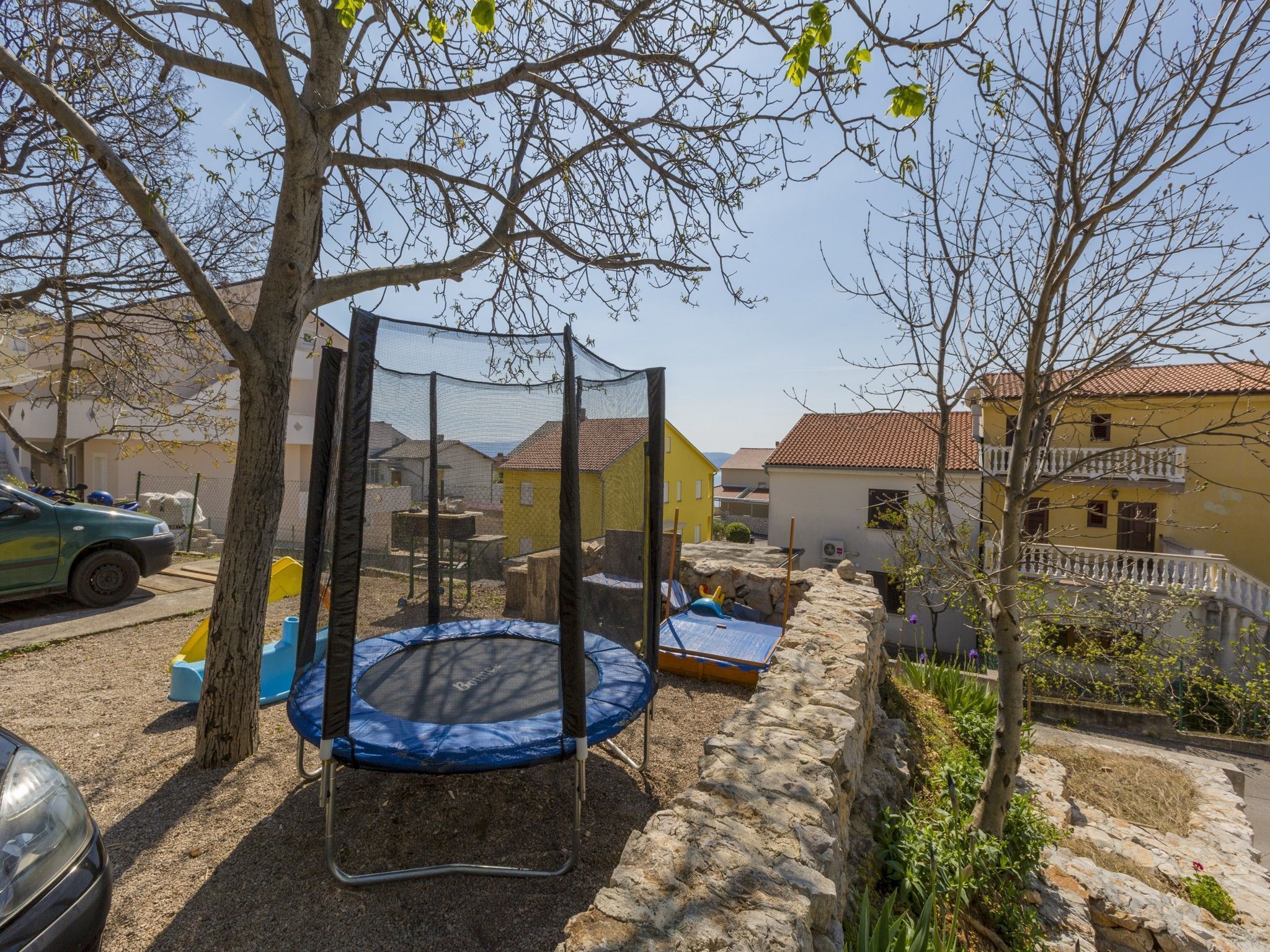 Un quartier résidentiel avec un trampoline, un arbre et un mur de pierre.