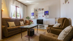A living room with a sofa, armchair, coffee table, TV, and decorative items. - Apartments Lilin (Crikvenica)
