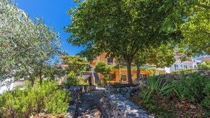 A stone staircase leading up to a building with a balcony, surrounded by greenery and trees. - Apartments Lilin (Crikvenica)