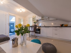 Une cuisine moderne avec des meubles blancs, un coin repas doté d’une table blanche, et une vue sur la salle de bain adjacente.