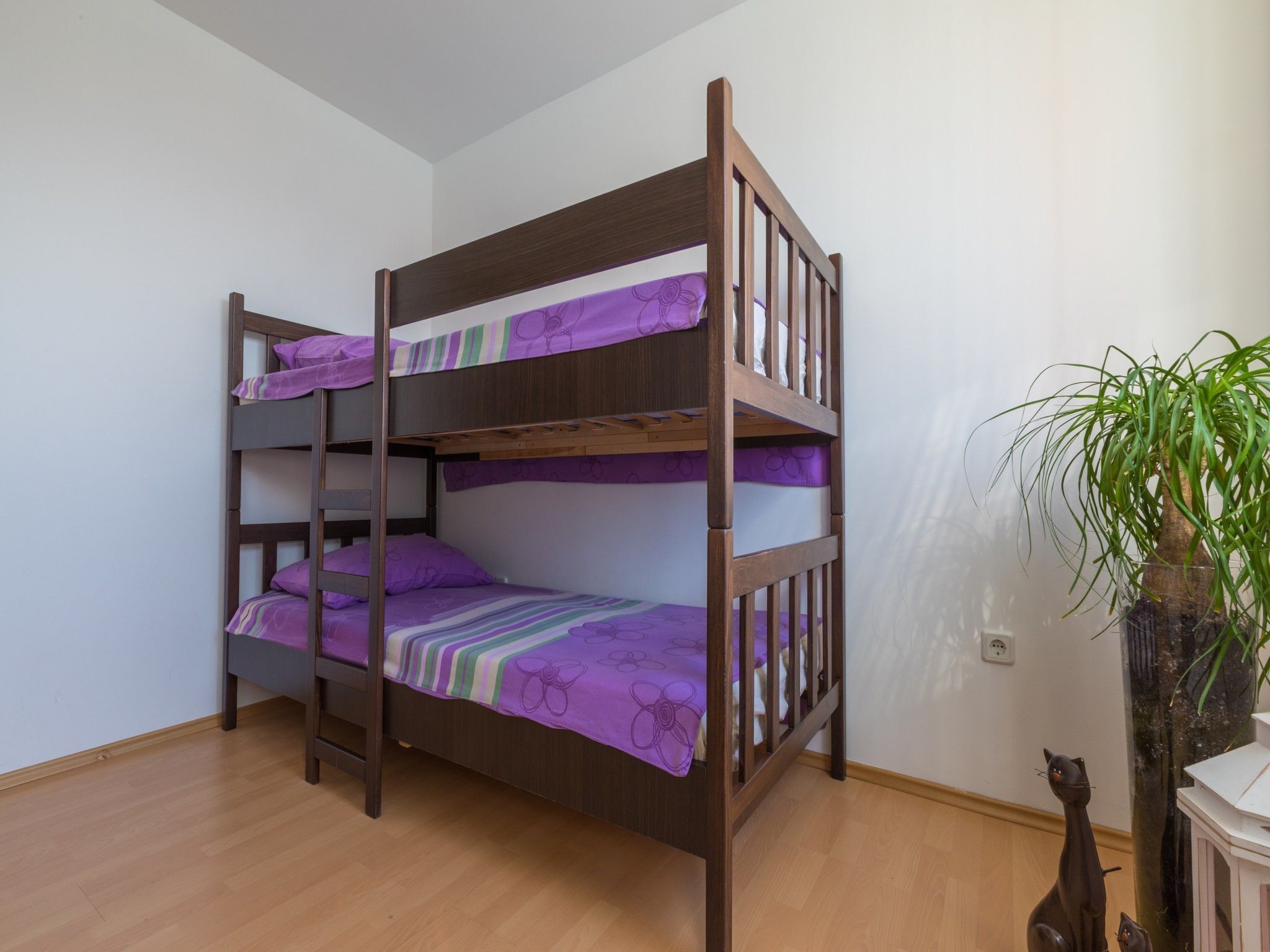 A bunk bed with purple bedding in a room with wooden flooring and a potted plant.