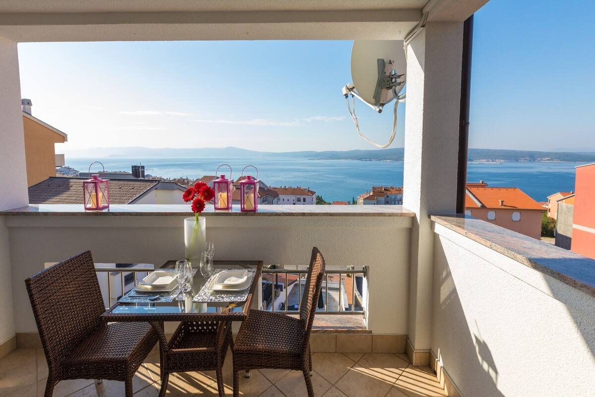 A balcony with a table set for two, overlooking a coastal view.