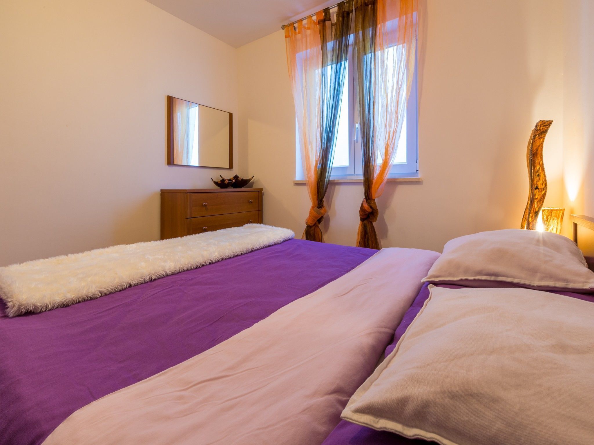 Un dormitorio con una cama grande, un aparador de madera, un espejo y una ventana con cortinas.