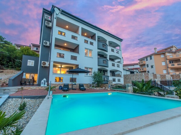 Un edificio de varios pisos con balcones, piscina y mobiliario exterior.
