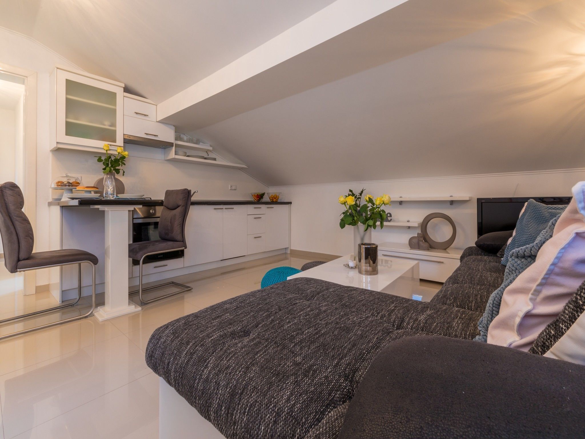 A modern apartment with a kitchenette, a dining area, and a living room with a sofa and a TV.