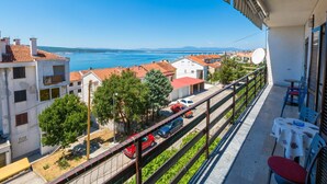 A balcony with a view of a coastal town, a street with parked cars, and a satellite dish. - Apartments Ankica (Crikvenica)