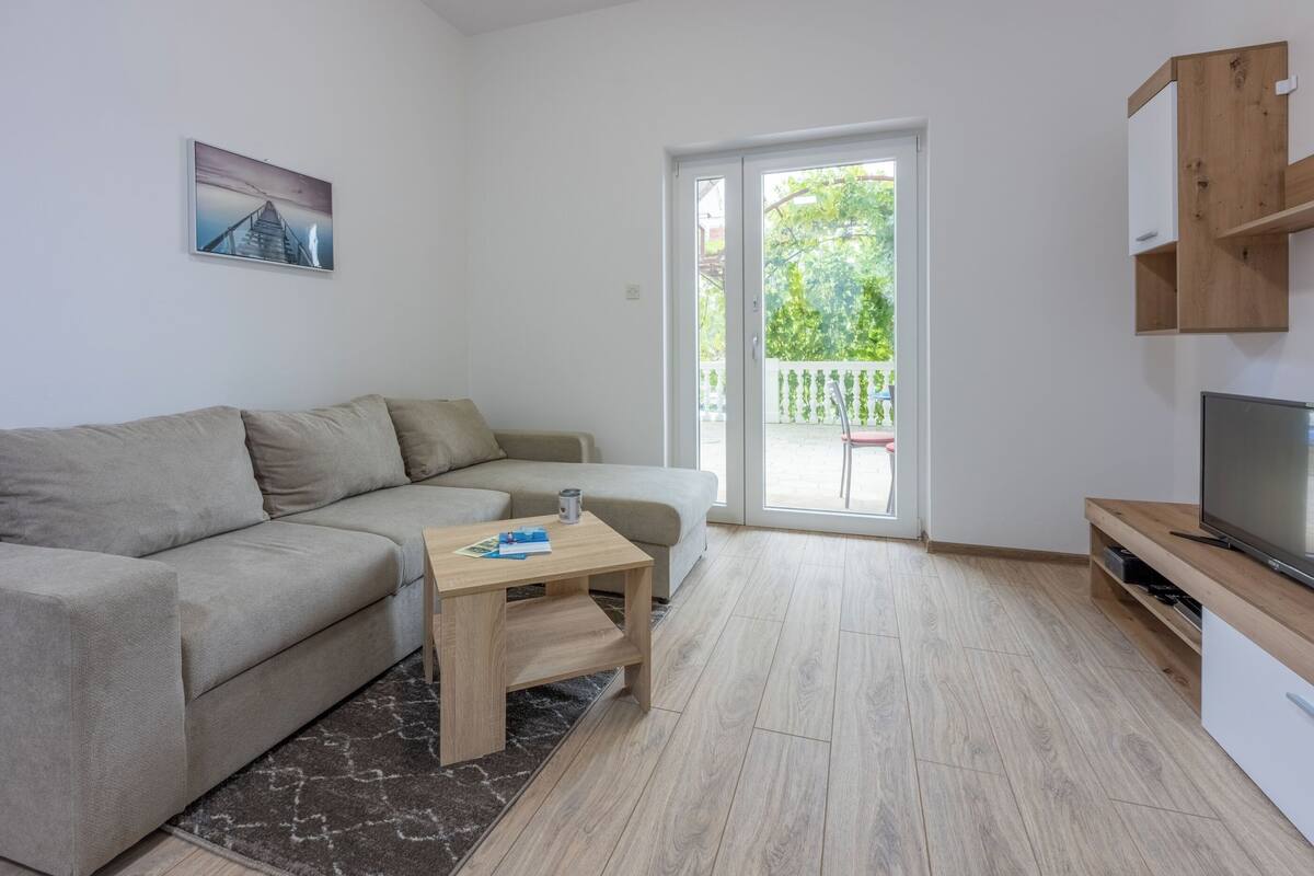 A modern living room with a sofa, a coffee table, a TV, and a sliding glass door leading to a balcony.