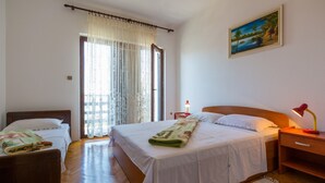 A hotel room with two beds, a wooden floor, a painting on the wall, and a window with curtains. - Apartments Ankica (Crikvenica)