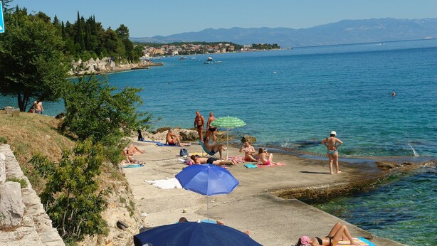 A beach with people sunbathing and swimming, a pier extending into the water, and a mountainous backdrop. - Apartments Ankica (Crikvenica)