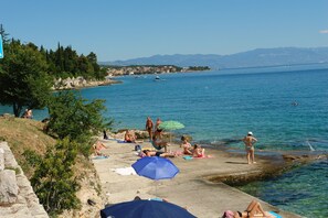 A beach with people sunbathing and swimming, a pier extending into the water, and a mountainous backdrop. - Apartments Ankica (Crikvenica)