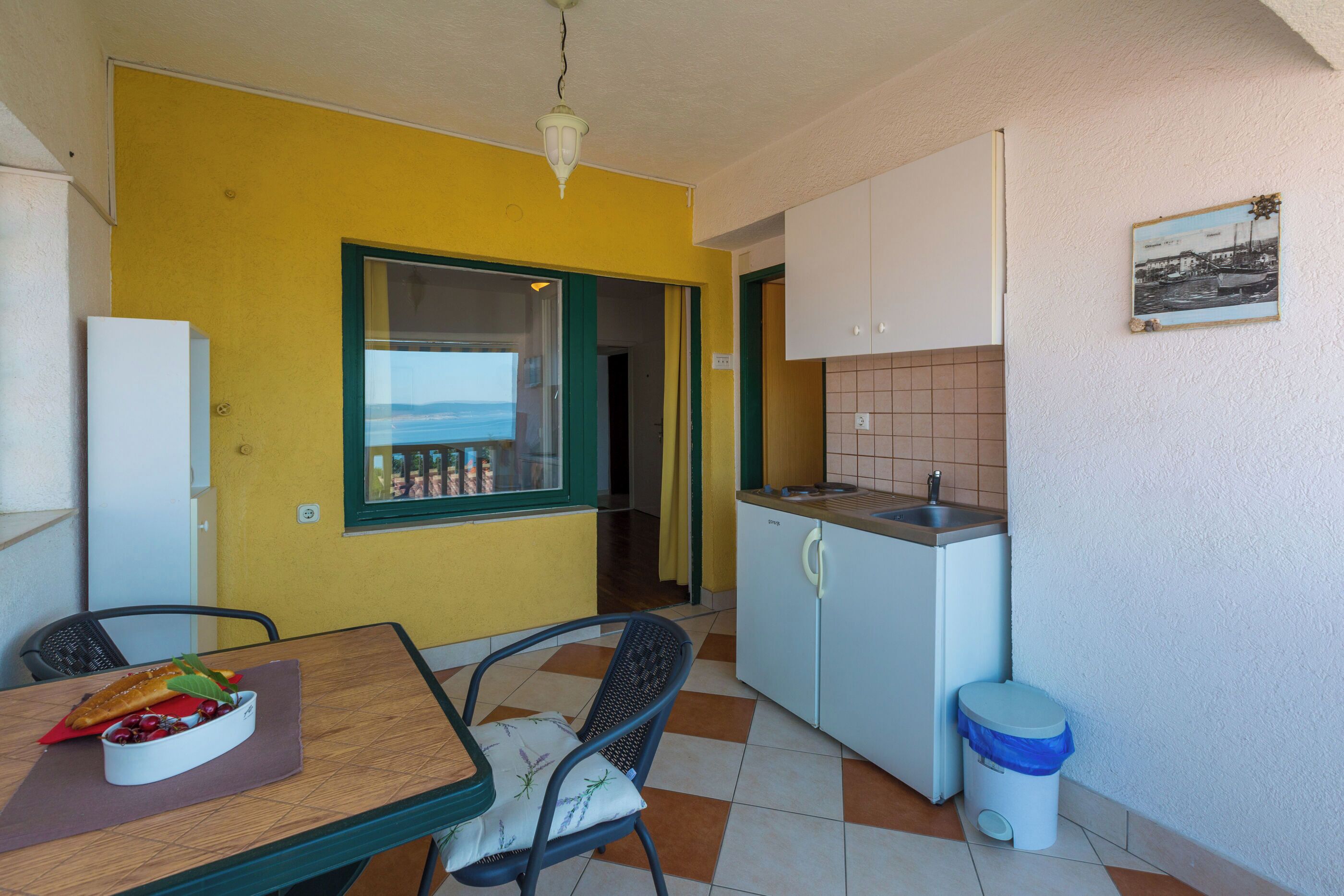 A compact kitchen with a dining area, a view through a window, and a small trash bin.