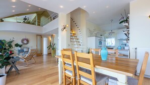 Een ruime eethoek met een houten tafel en stoelen, een trap die naar een hoger niveau leidt en een keuken op de achtergrond.