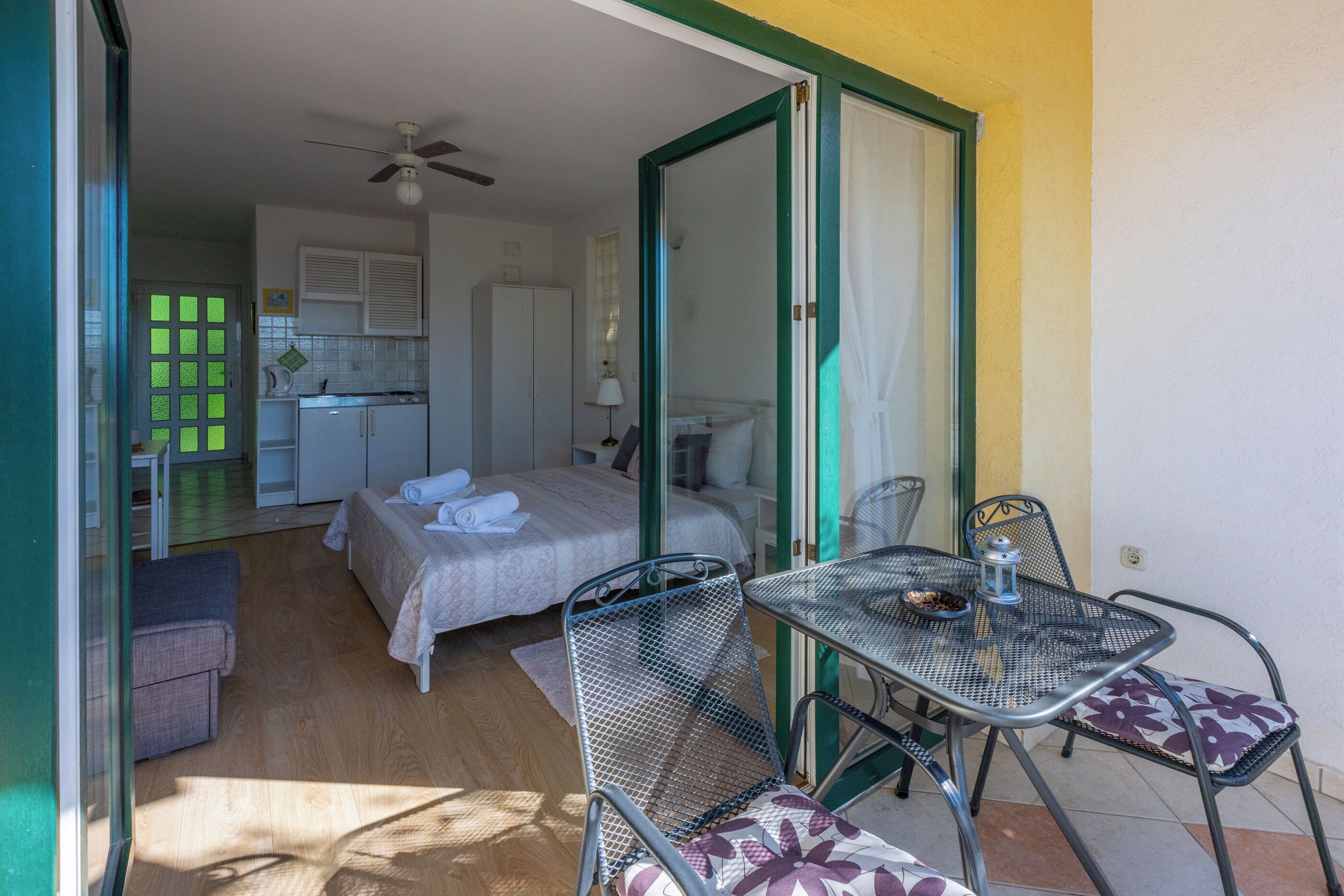 Una habitación con cama, una kitchenette pequeña, una mesa de comedor con sillas y un ventilador de techo.