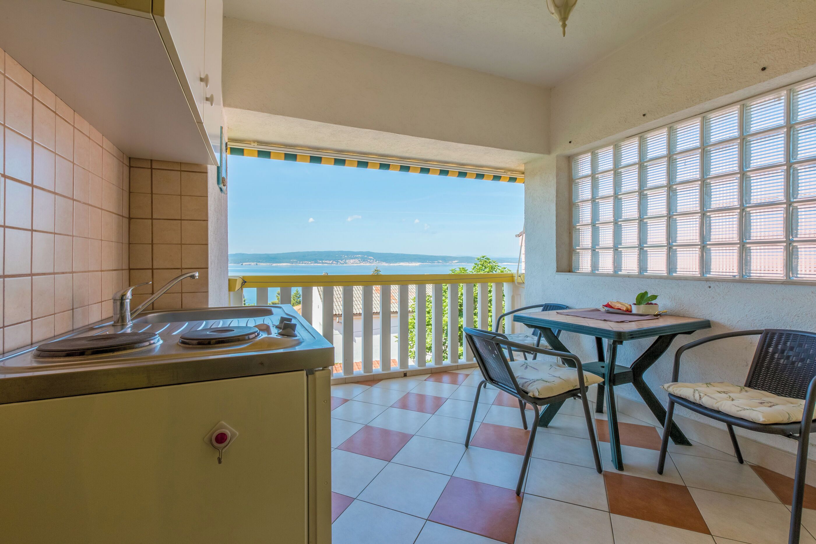 Une cuisine avec vue sur la mer, une table à manger avec des chaises et un balcon doté d’une balustrade.