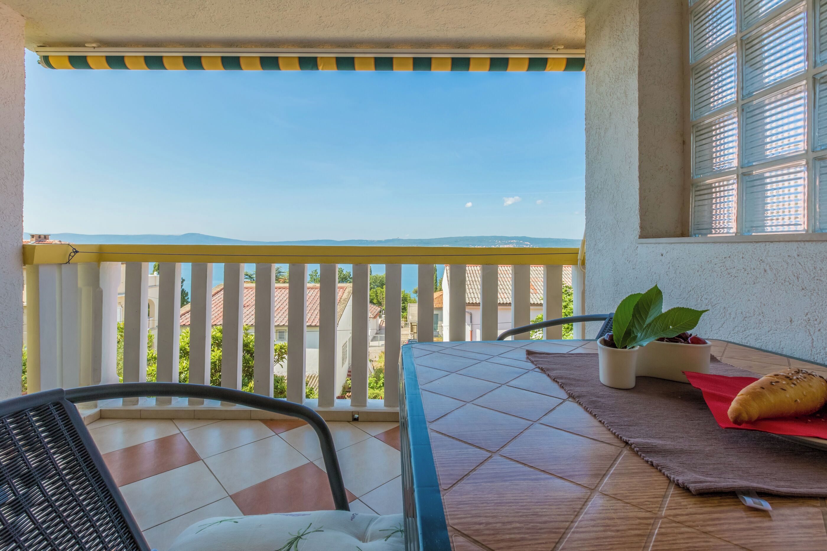 A balcony with a view of distant buildings and mountains, a table with a napkin and bread, and a potted plant.