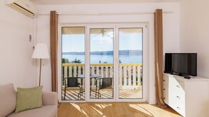 Een kamer met een bank, een televisie, een balkon met uitzicht op zee en een plafondventilator.
