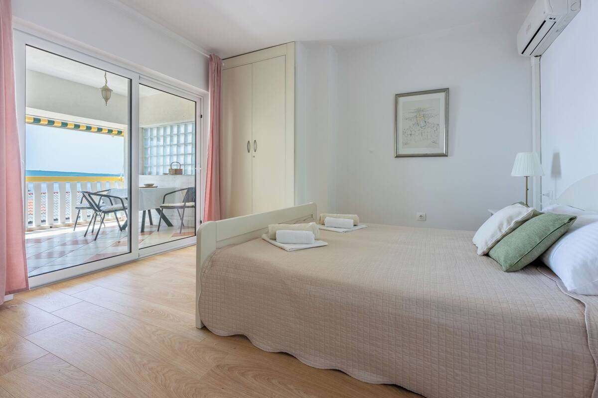 A bedroom with a bed, a wardrobe, a balcony, and a view of the outside.