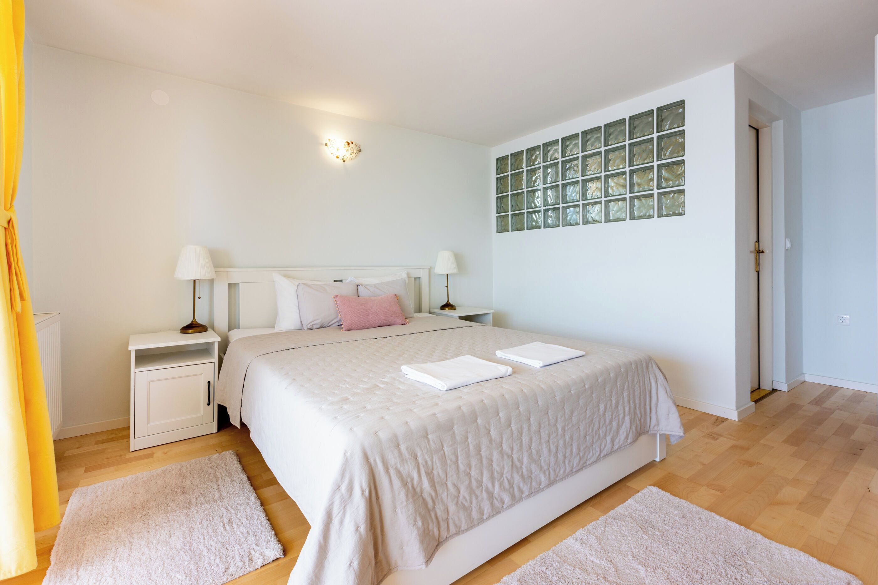 A bedroom with a large bed, two bedside tables with lamps, a nightstand, a window with green glass panes, and a door.