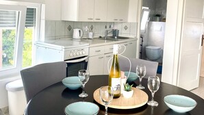 A modern kitchen with white cabinets, a dining table with blue bowls, and a bottle of wine. - Apartment Seka (Sabunike)