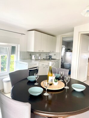 A modern kitchen with white cabinets, a dining table with blue bowls, and a bottle of wine.