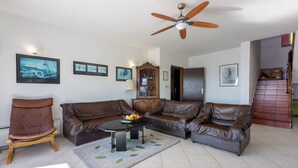 A living room with a brown leather sofa, a wooden chair, a coffee table with fruit, and a ceiling fan.