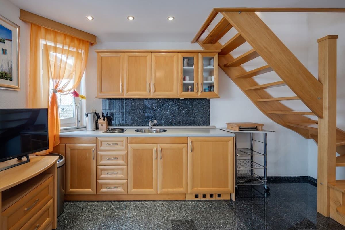 A compact kitchen with wooden cabinets, a granite countertop, a built-in sink, and a wooden staircase.