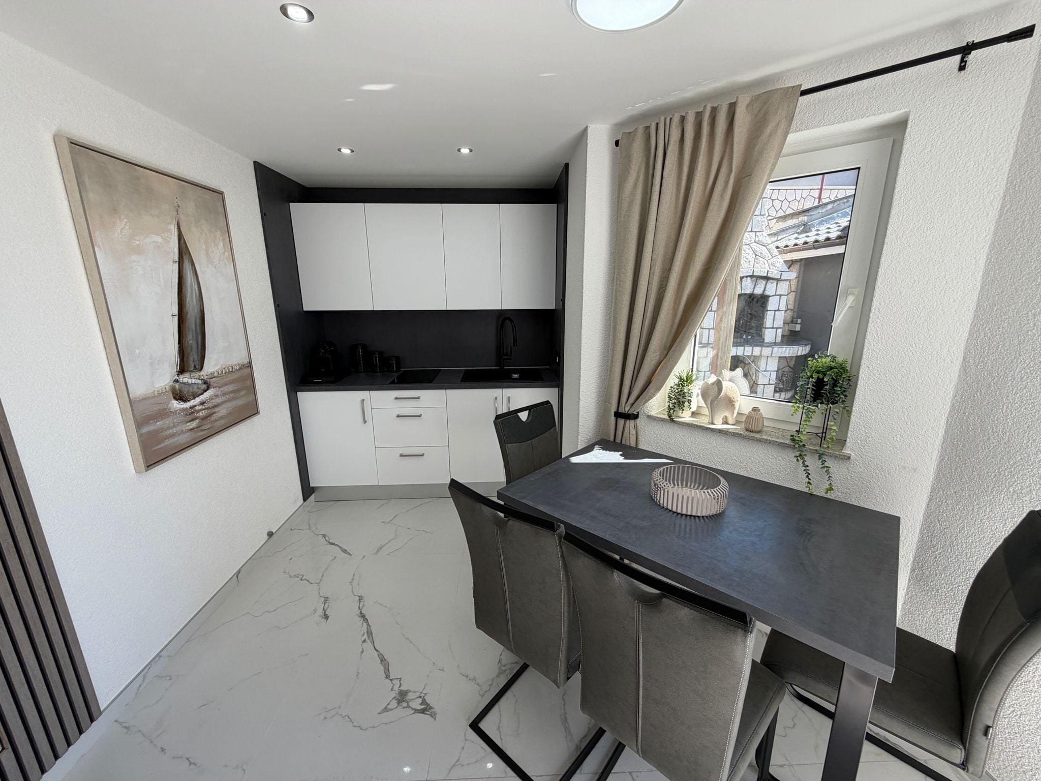 A compact kitchen with white cabinets, a black countertop, and a window with curtains.