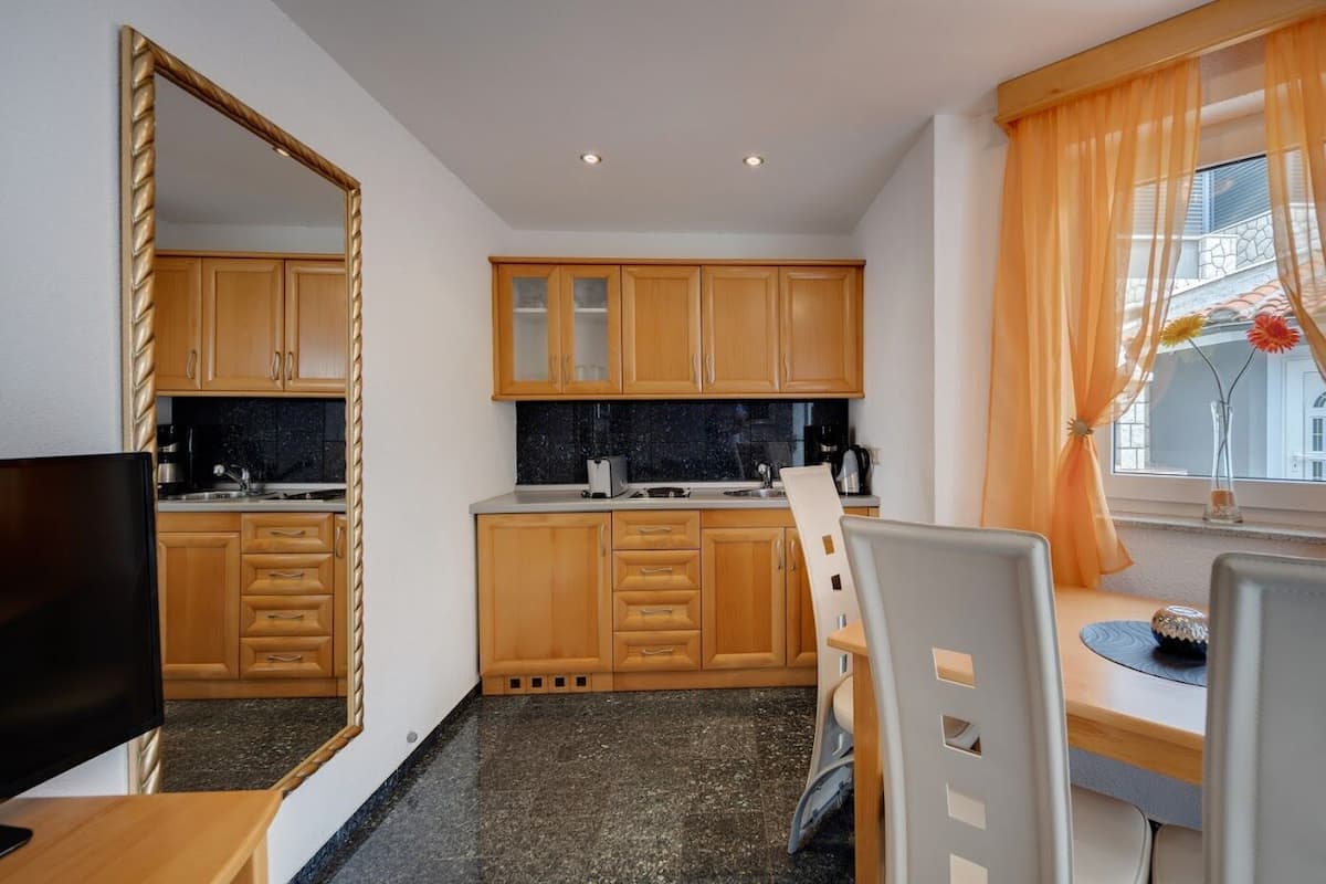 A compact kitchen with wooden cabinets, a granite countertop, and a dining area with a chair and table.