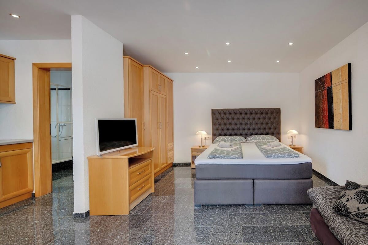 A bedroom with a bed, a TV on a stand, wooden cabinets, and a painting on the wall.